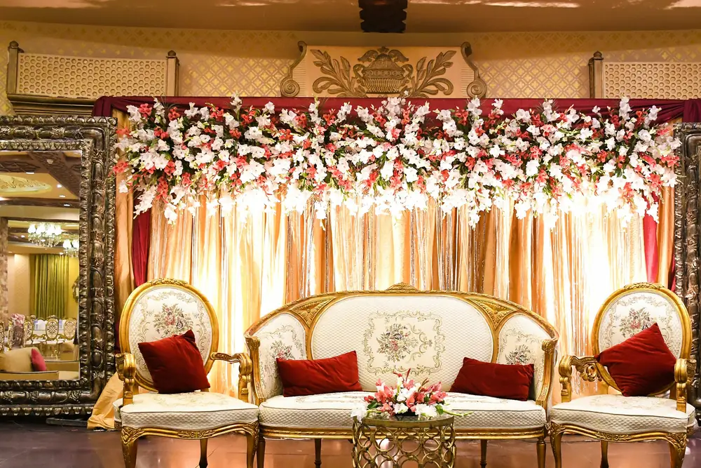 A candlelit wedding stage with an ivory and gold sofa and a canopy of roses