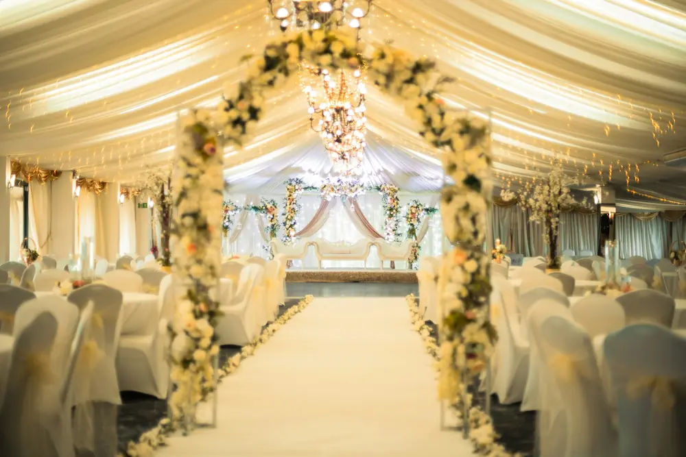An ivory aisle beneath floral archways leading towards a dressed stage