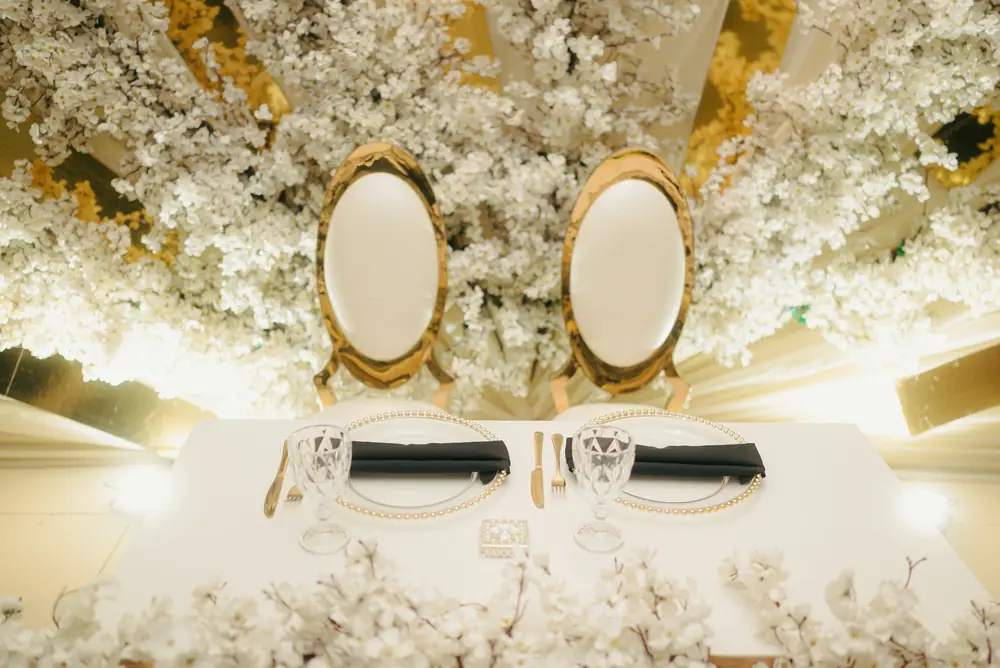 Two gold-framed chairs at a head table beneath a canopy of white blossom