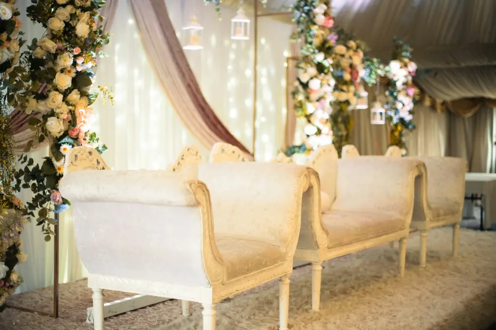 Ivory carved sofas on a stage beneath fairy lights and trailing florals