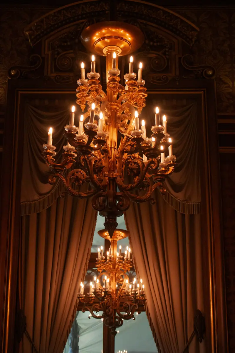 An ornate golden chandelier with lit candles above heavy drapery