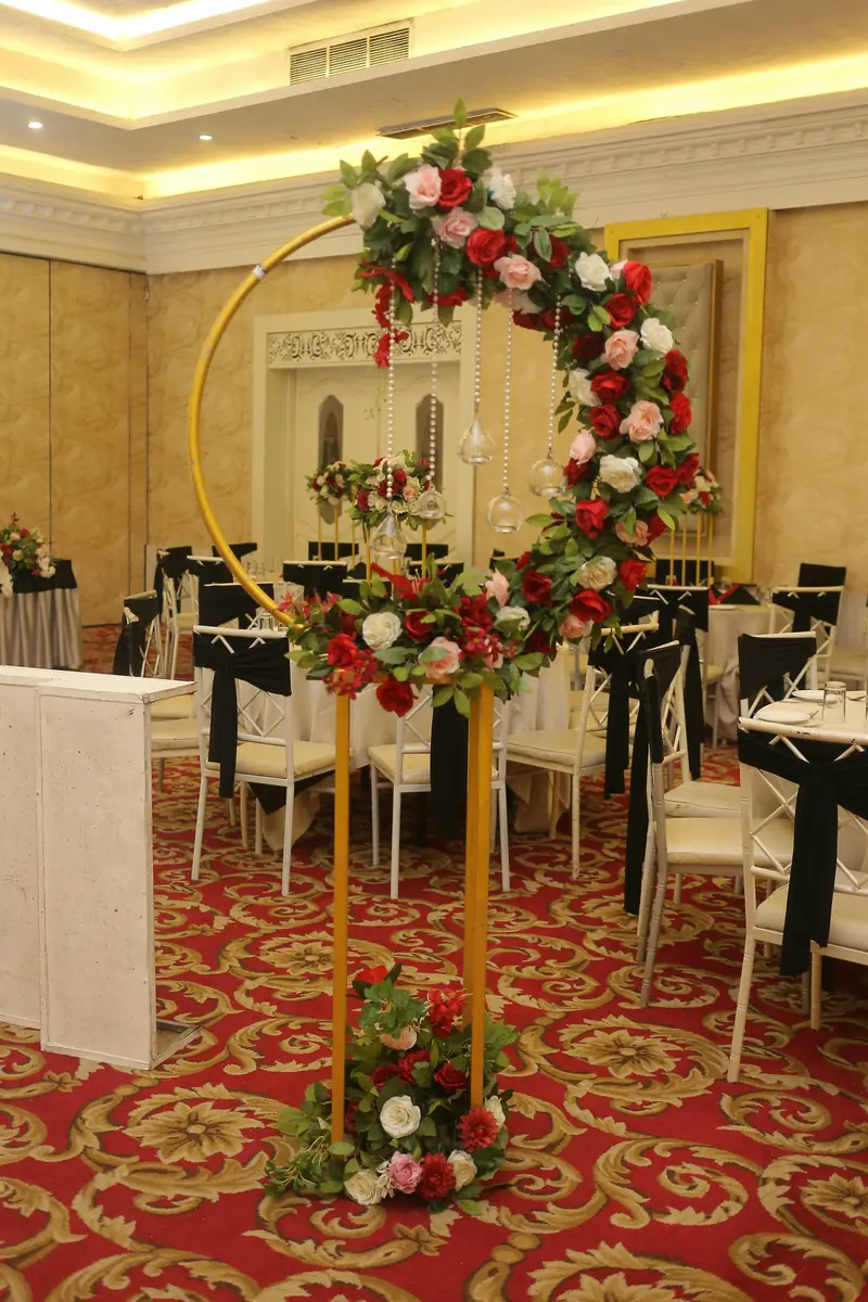 A gold circular arch dressed with red and ivory roses in a banquet hall
