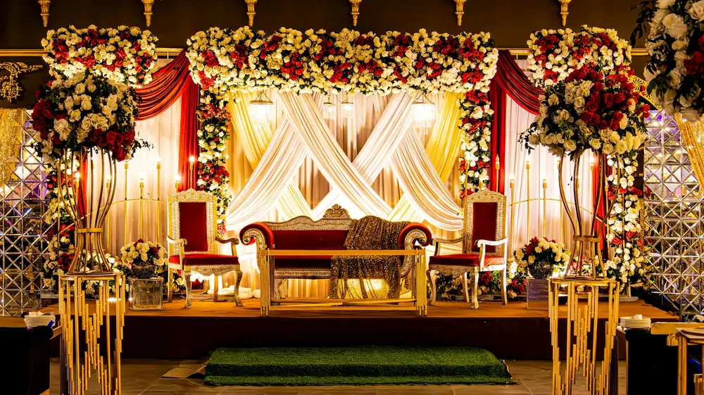 A red and gold wedding stage framed by roses, ivory drapery and gilded chairs