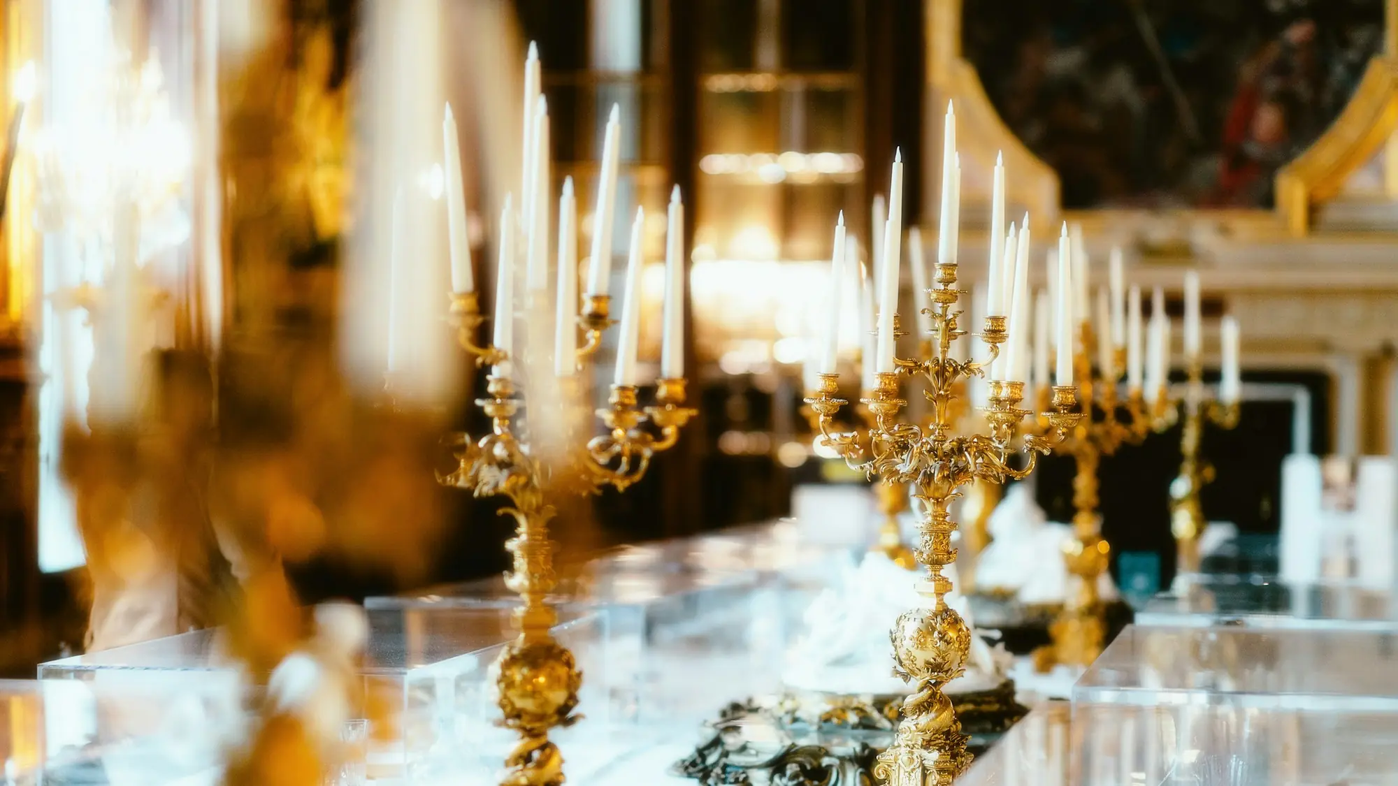 Gold candelabra with tall ivory candles glowing along a dressed reception table