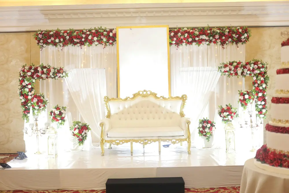 An ivory tufted sofa with gold detailing on a stage framed by red and white roses